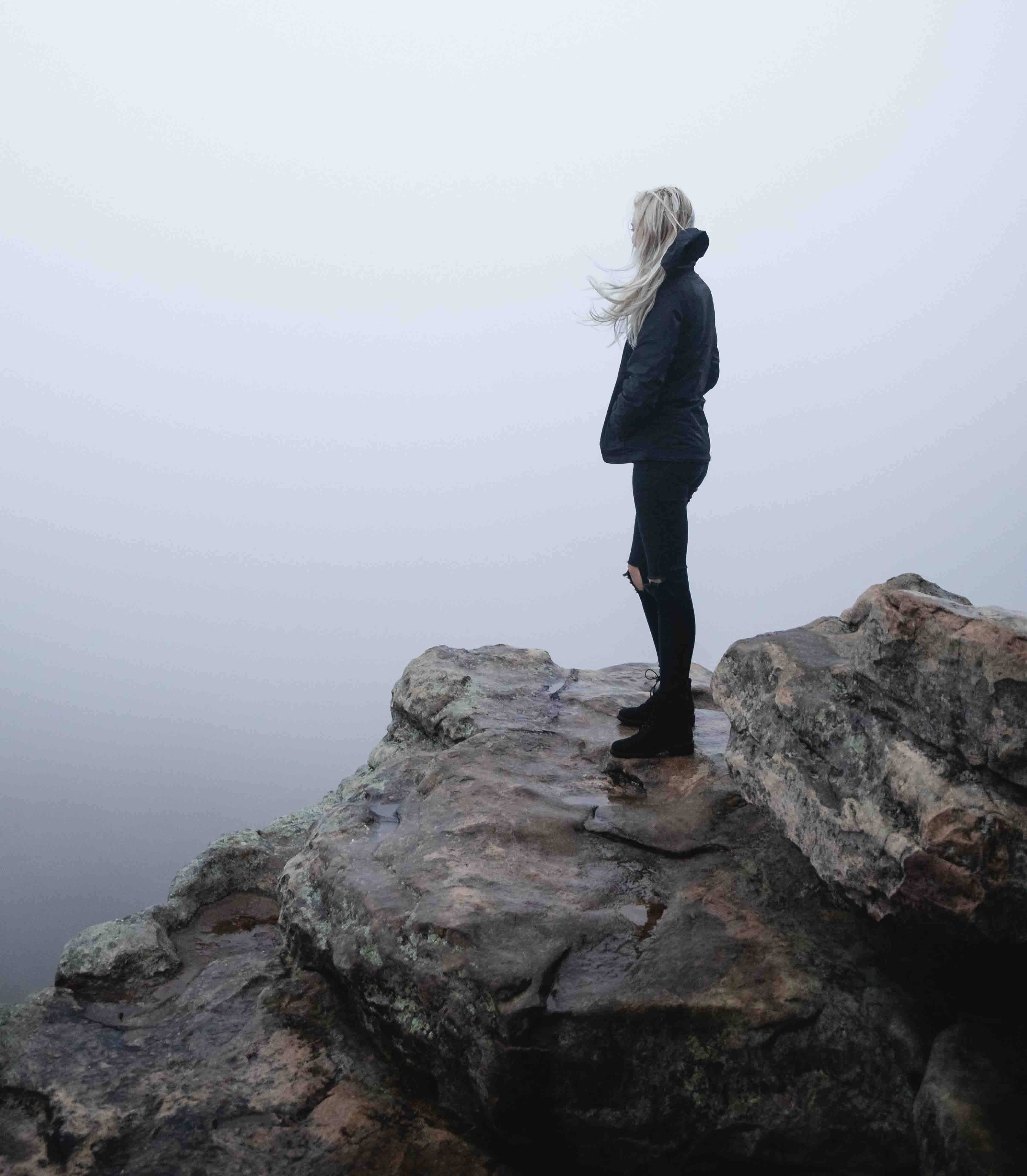 woman looking into the fog on top of a rock